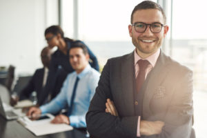 profeshh 56128033 - confident smiling business executive with folded arms near conference table with three co-workers discussing something in large bright office room
